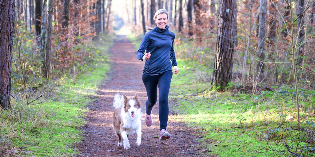 Frau joggt mit Hund im Wald