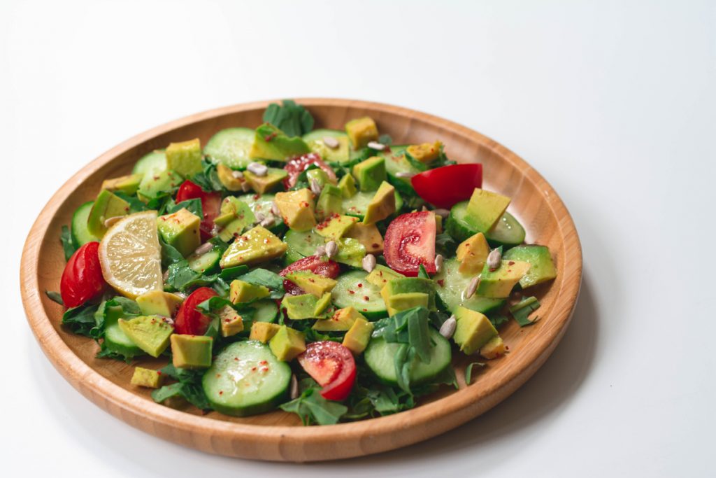 Gesunder Salat mit Avocado, Gurke und Tomate auf einem Holzteller