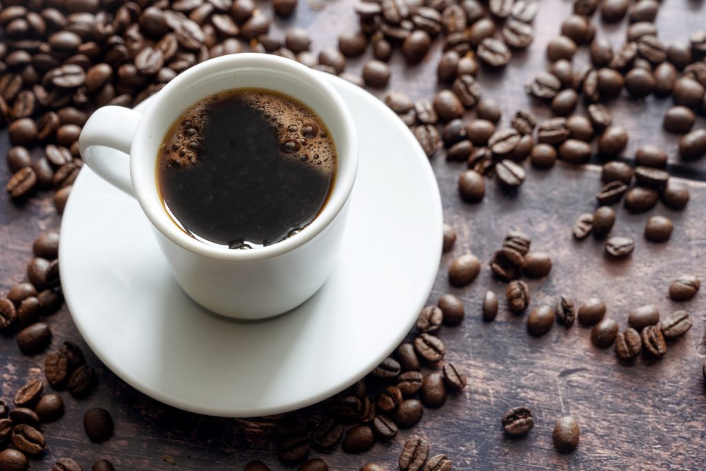 weiße Kaffeetasse mit schwarzem Kaffee umgeben von Kaffeebohnen
