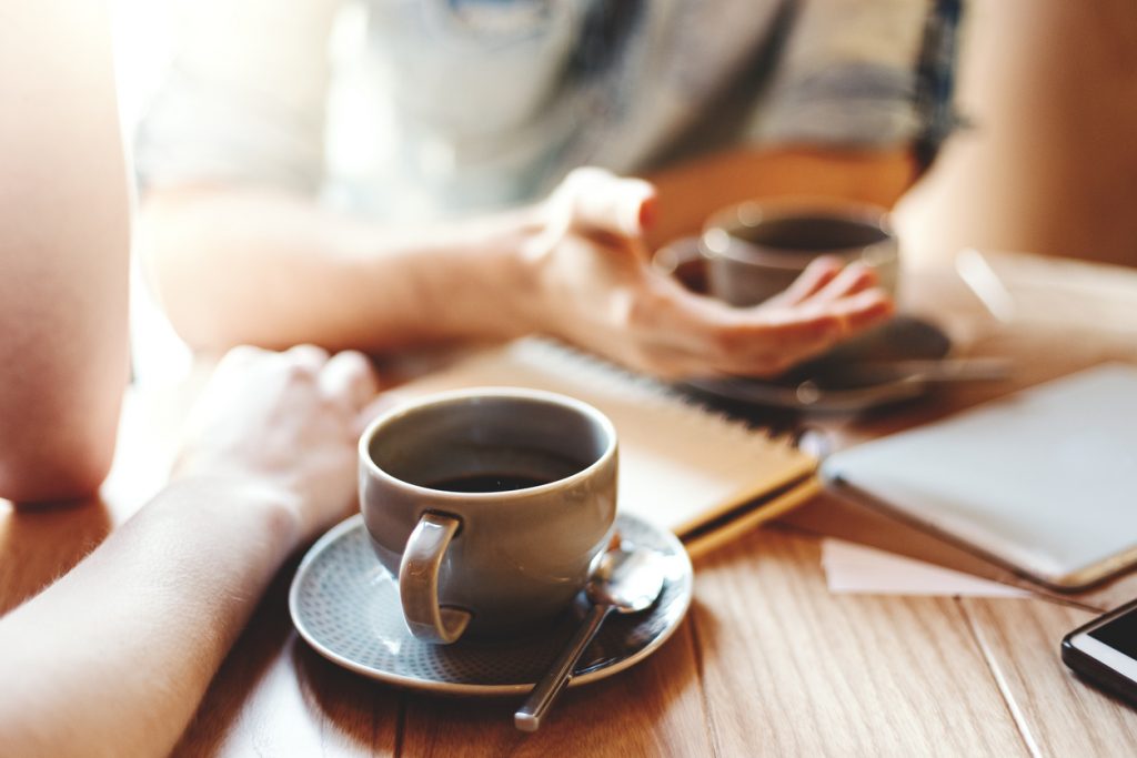 zwei Kaffeetassen auf einem Holztisch bei einem Gespräch zwischen zwei Personen